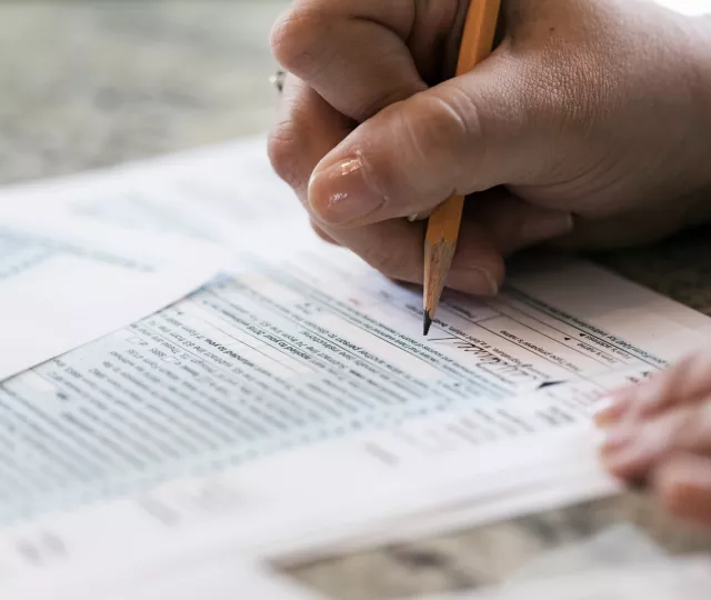 Photo of a person's hand using a pencil to fill out a tax form.