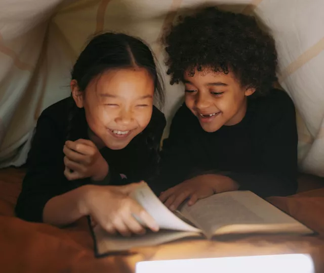 2 young children reading under a blanket fort