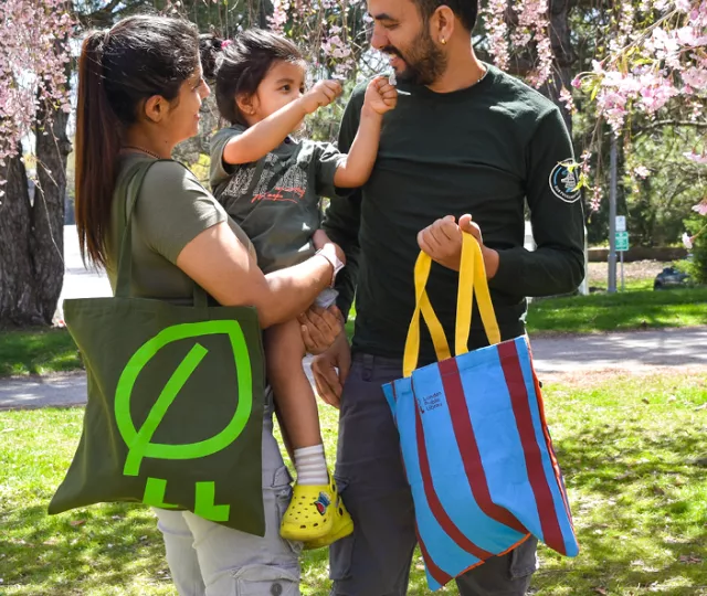 Family standing in a park holding London Public Library tote bags.