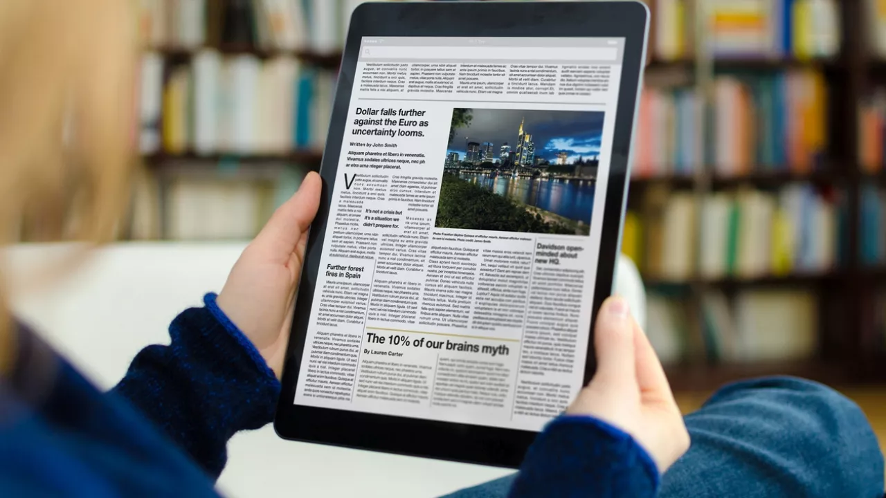 Photo of person's hands holding a large tablet with a digital newspaper displayed.