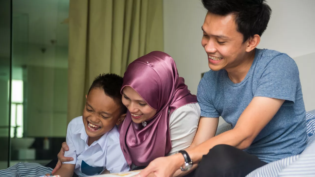 Photo of Mother and father with child on bed reading picture book