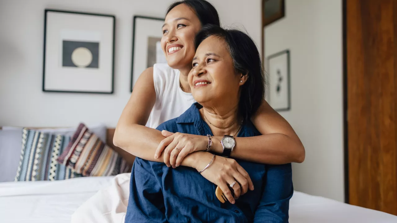 Woman standing behind an older woman with her arms around her.