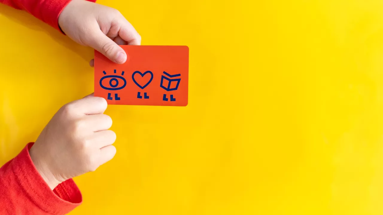 Child holding red library card against a yellow background