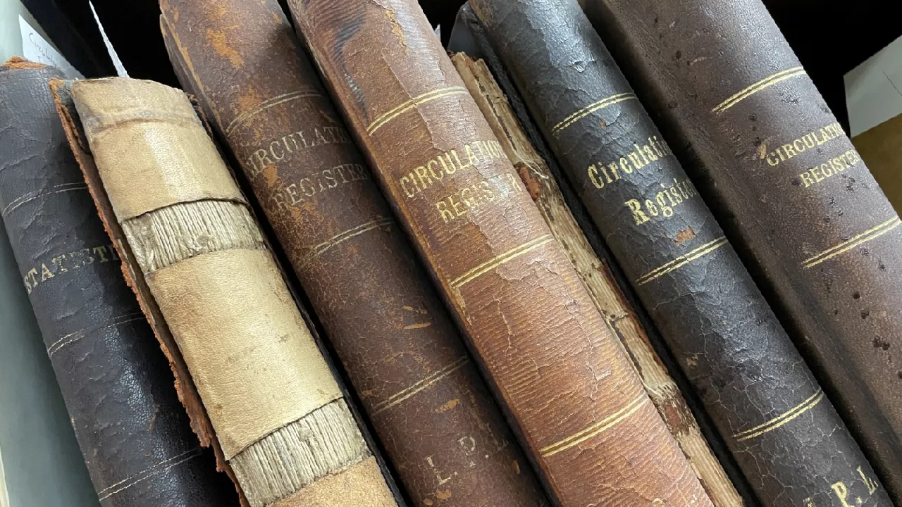 Photo of old leather bound circulation registers sitting on a shelf in the London Room