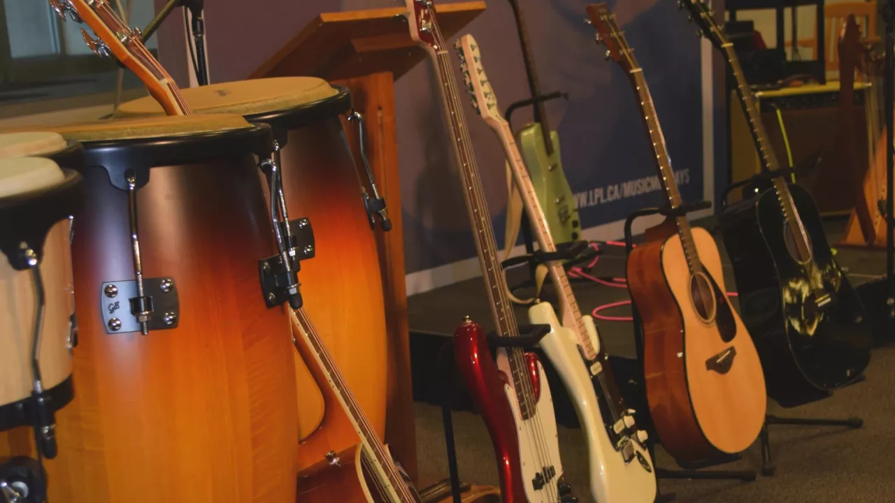 Photo of several acoustic and electric guitars lines up in a row. In the front ar large conga drums.