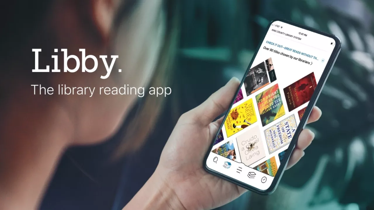 Photo of a youth looking at a phone displaying ebooks. On top of the photo are the words Libby The Library reading app.