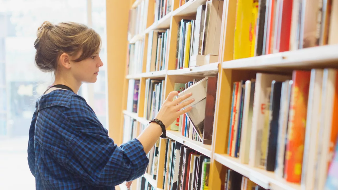 Photo of a young woman taking a book from a shelf at the library.