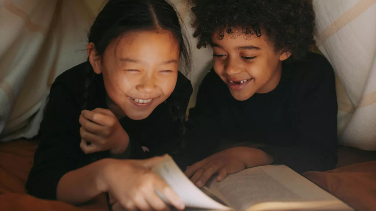 2 young children reading under a blanket fort