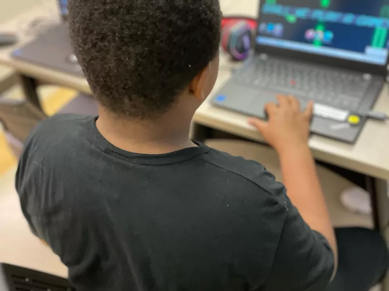 Photo of a youth sitting in front of a laptop at Sherwood Branch. In the background is a table with other laptops. 