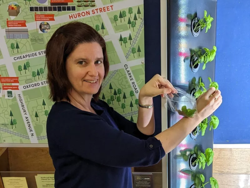 A photo of Beacock's Supervisor picking basil from their hydroponic growing station. In the background is a map of the neighbourhood.