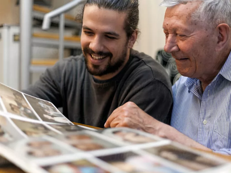 Photo of a bearded younger man and an older man looking at a photo album together and smiling.