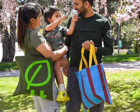 Family standing in a park holding London Public Library tote bags.