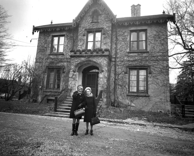 Black and white photo of a couple standing in front of a large manor house