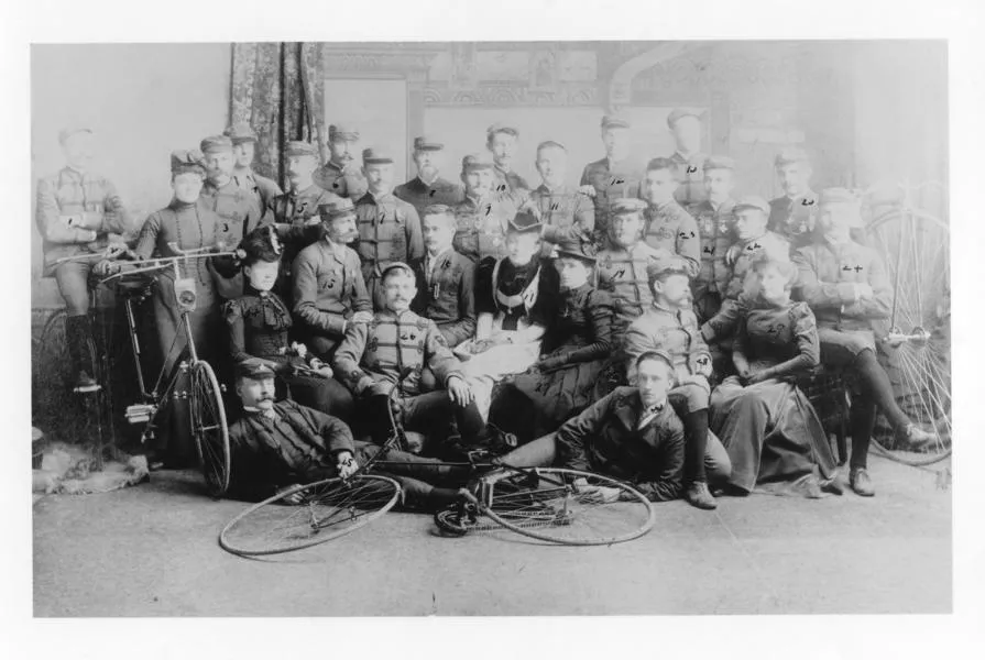 black and white photo of men sitting in a group together with bicycles