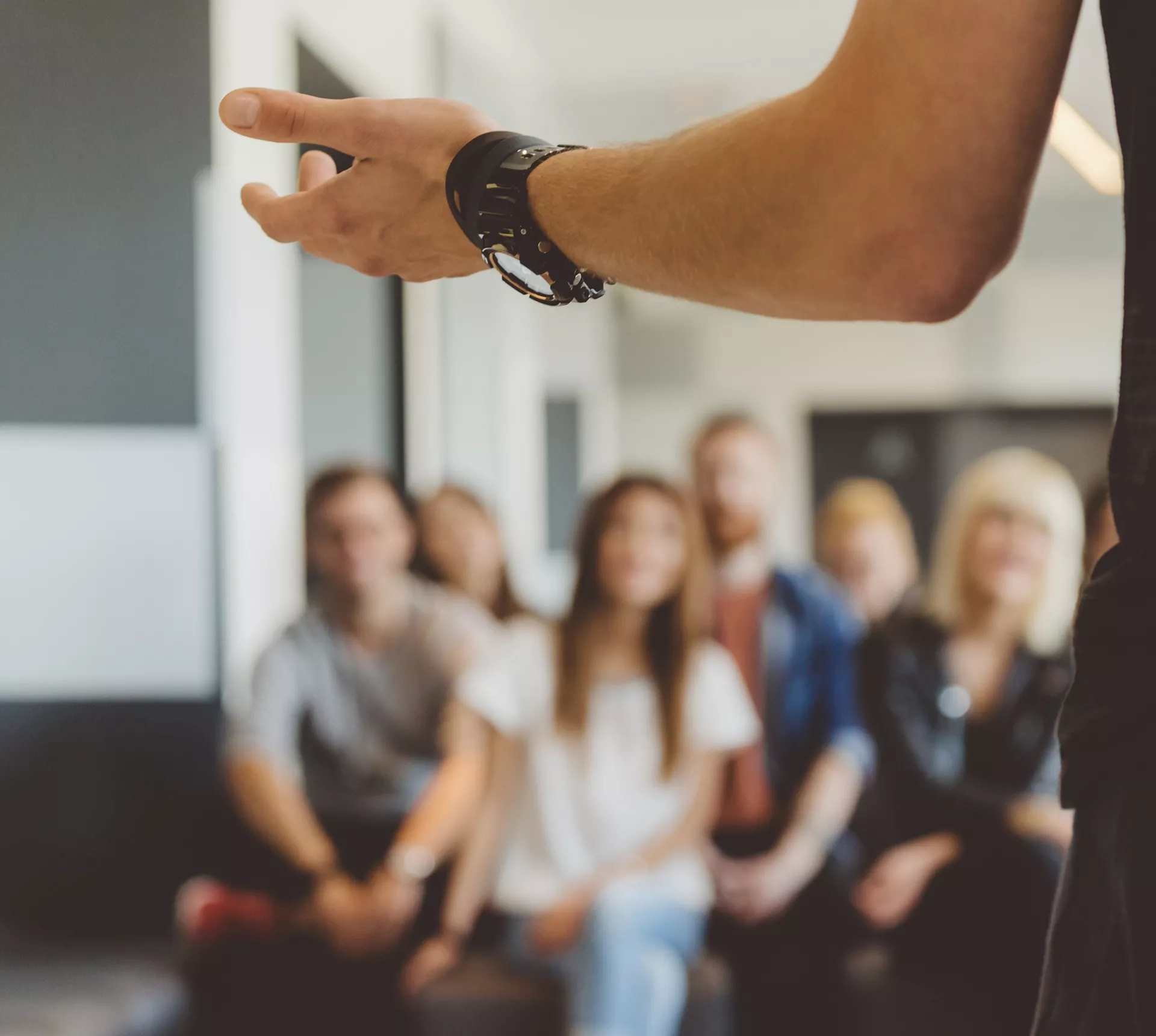 Photo of a group of people sitting in a room and looking at a person standing at the front.